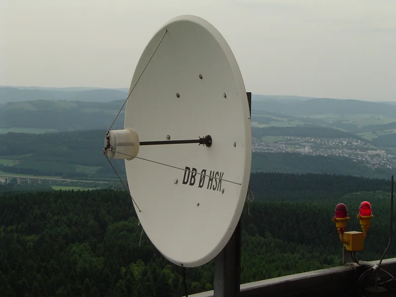 Mała biała antena paraboliczna z napisem DB0HSK na tle zalesionych wzgórz