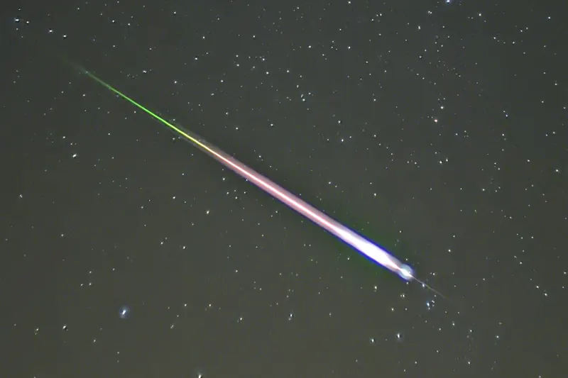 Jasny meteor z roju Leonid na tle gwiazd, za głową meteoru świecący, zielonkawy ślad