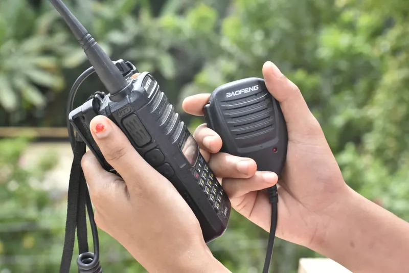 Dłonie trzymające radiotelefon Baofeng z anteną i mikrofonogłośnik na tle zieleni