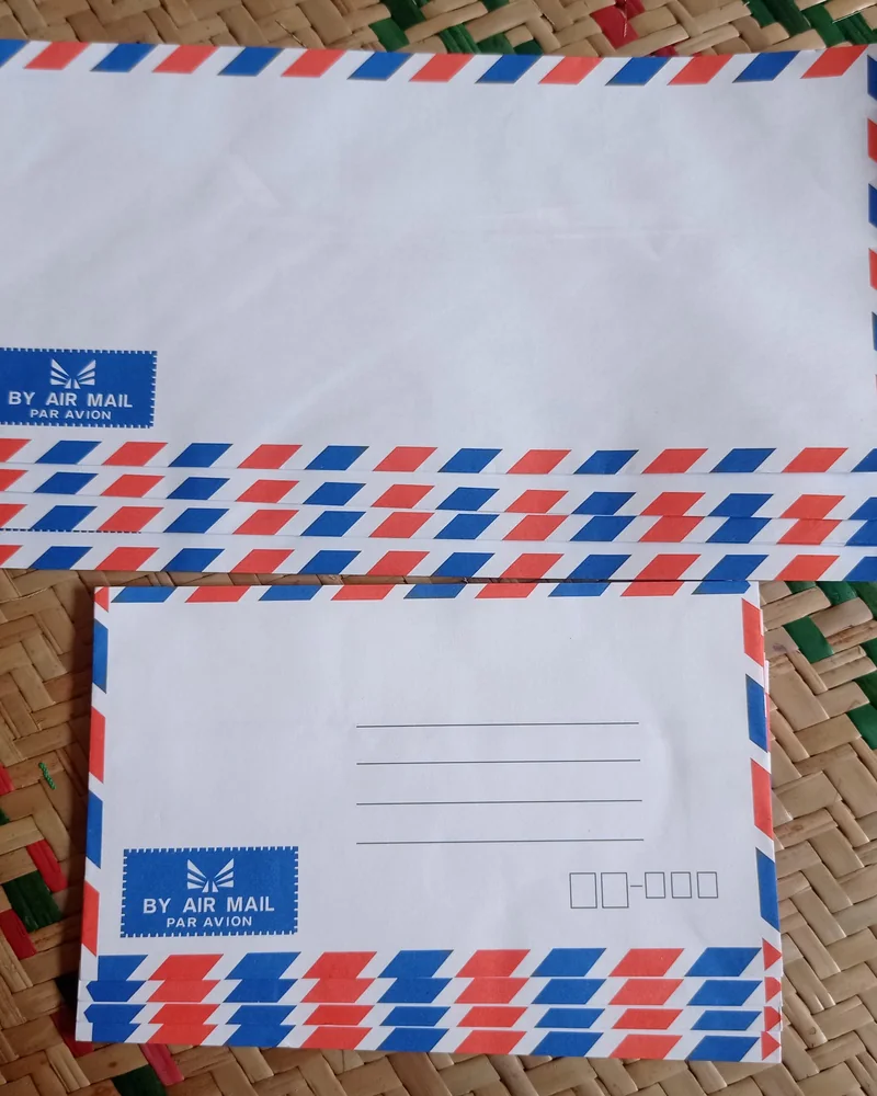 Dwa pliki pustych kopert lotniczych z biało-czerwono-niebieskim obramowaniem i naklejką By Air Mail na plecionej macie