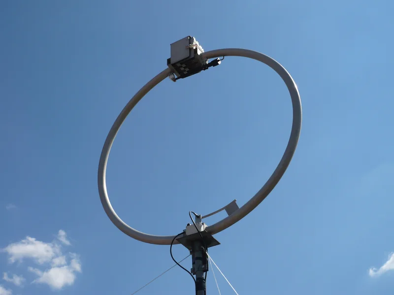 Okrągła antena pętlowa z rury aluminiowej na maszcie z odciągami, na tle błękitnego nieba.