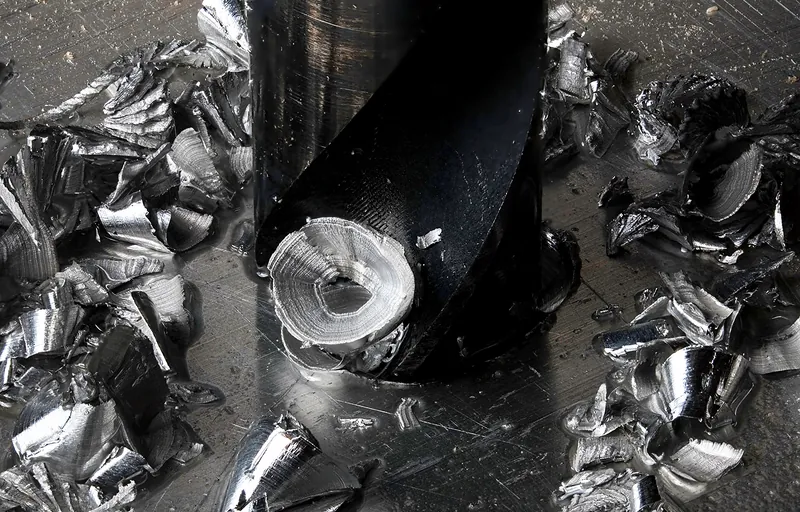 Wiertło ze stali szybkotnącej wchodzące w aluminium, dookoła błyszczące wióry i kropla smaru
